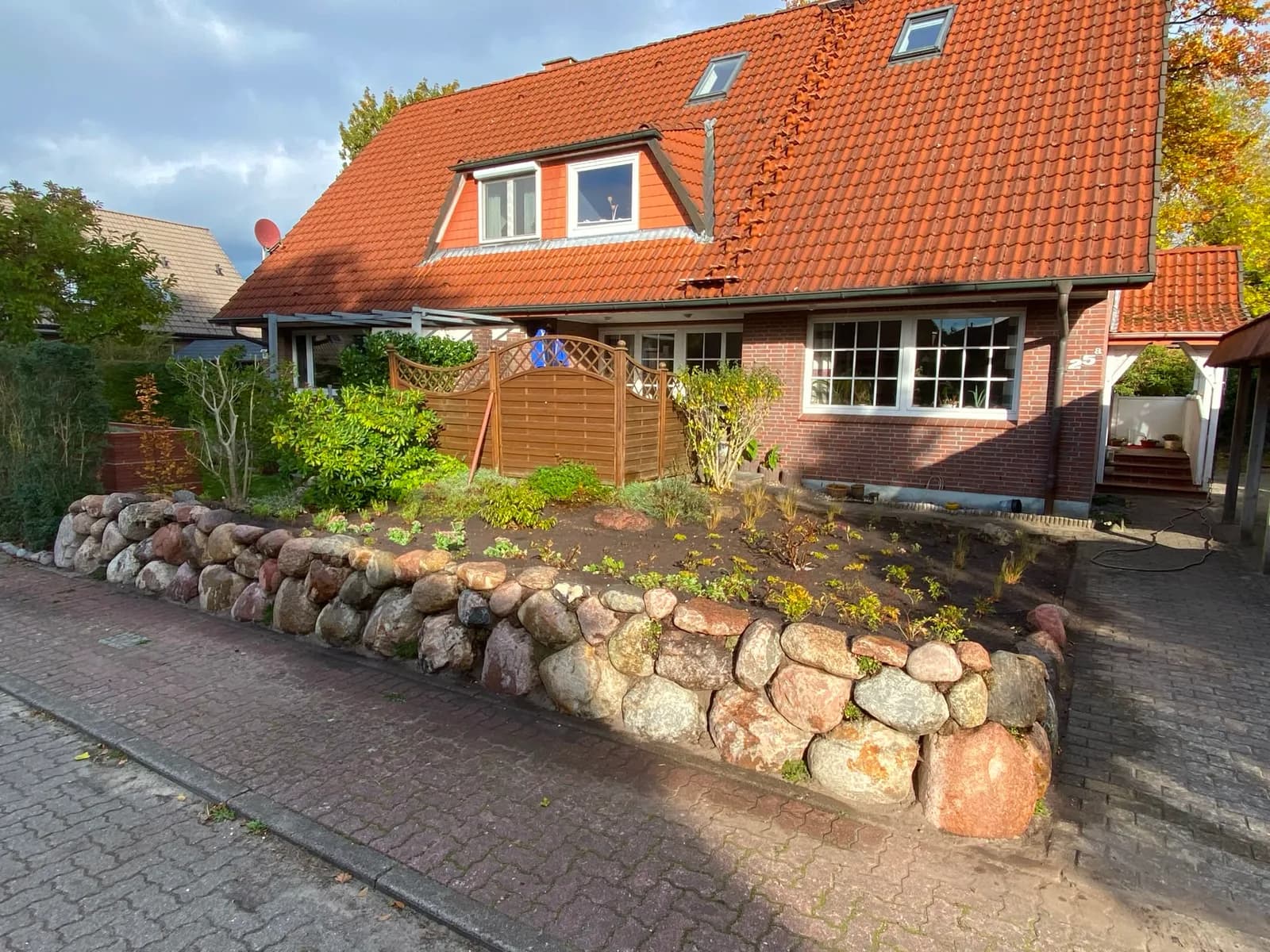 In Handarbeit gesetzte Findlingsmauer als Vorgarten-Hochbeet an einem Wohnhaus