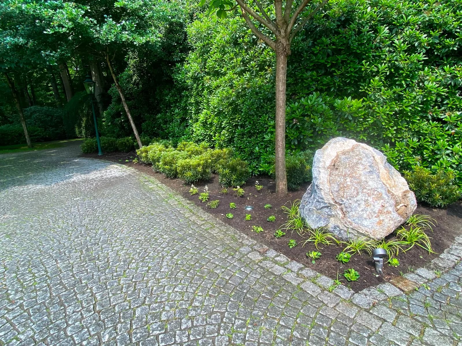 Gepflasterte Natursteinauffahrt mit Findling, Staudenbeet und Gartenbeleuchtung in Elmshorn
