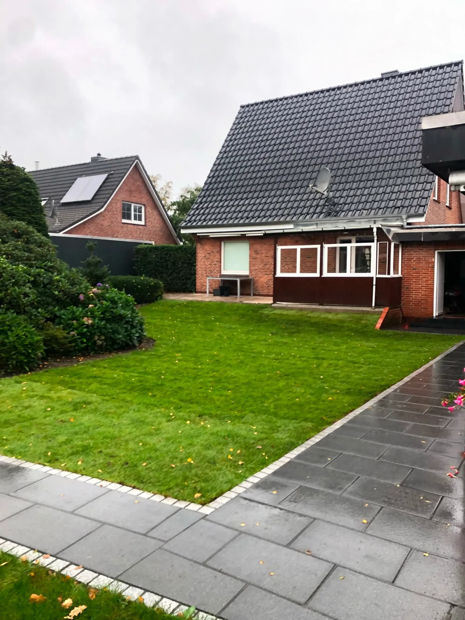 Frisch angelegter Rasen mit Granit-Randsteinen und Plattenweg an einem Wohnhaus