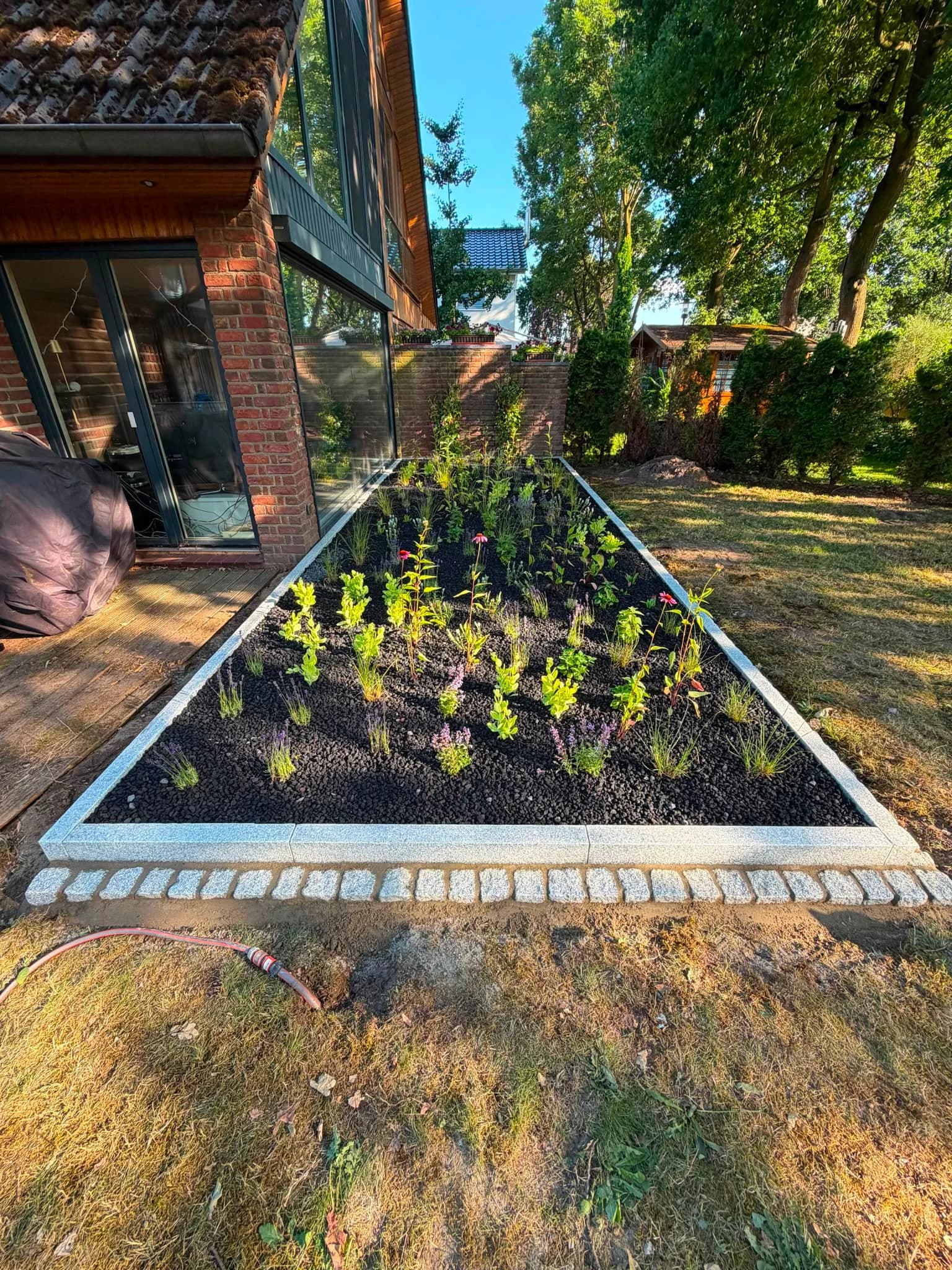 Neu angelegtes Staudenbeet mit Lavamulch und Granit-Einfassung entlang einer Terrasse
