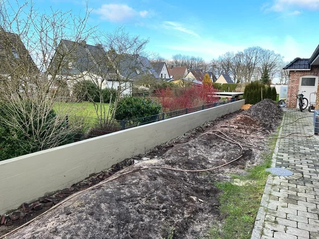 Neu errichtete, verputzte Stützmauer entlang der Grundstücksgrenze mit Pflasterweg